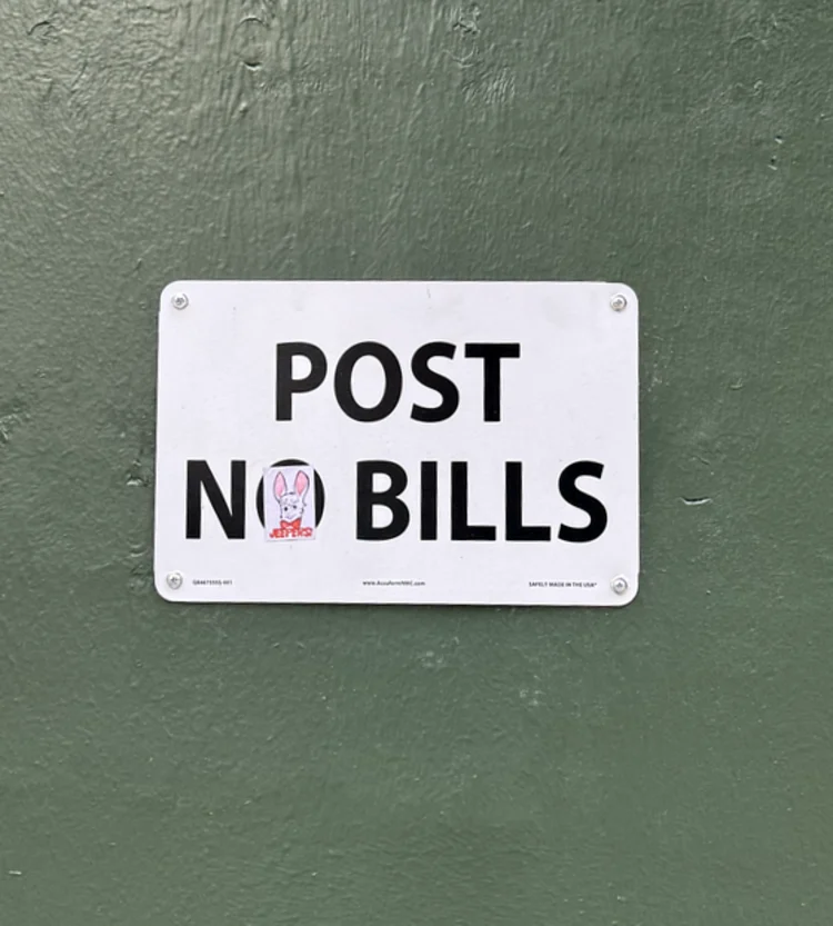 White plate sign on a light-green wall, straightened but marked with a small sticker.