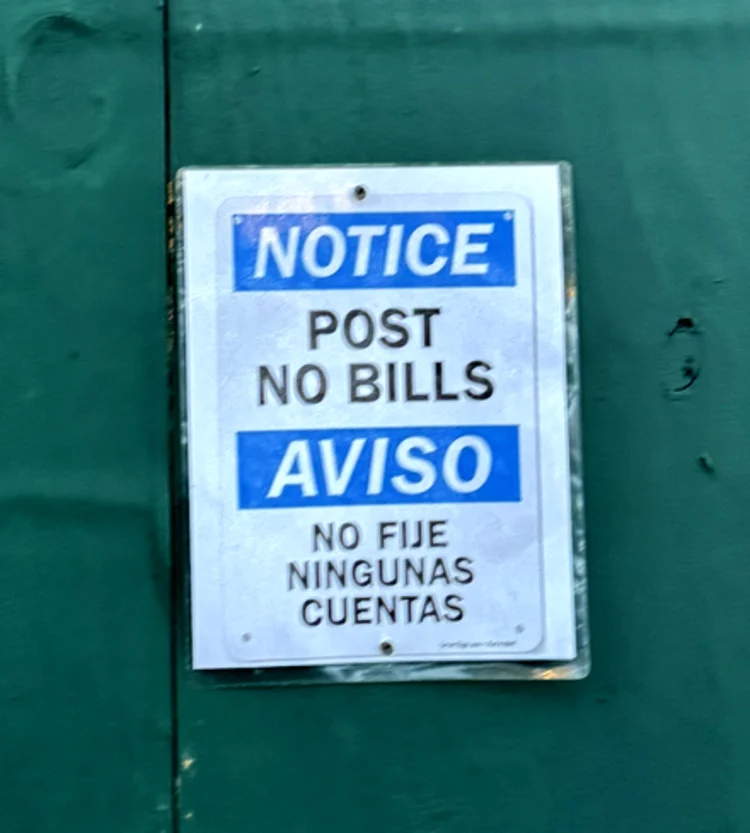 Weathered bilingual white plate sign mounted on a teal-painted door.